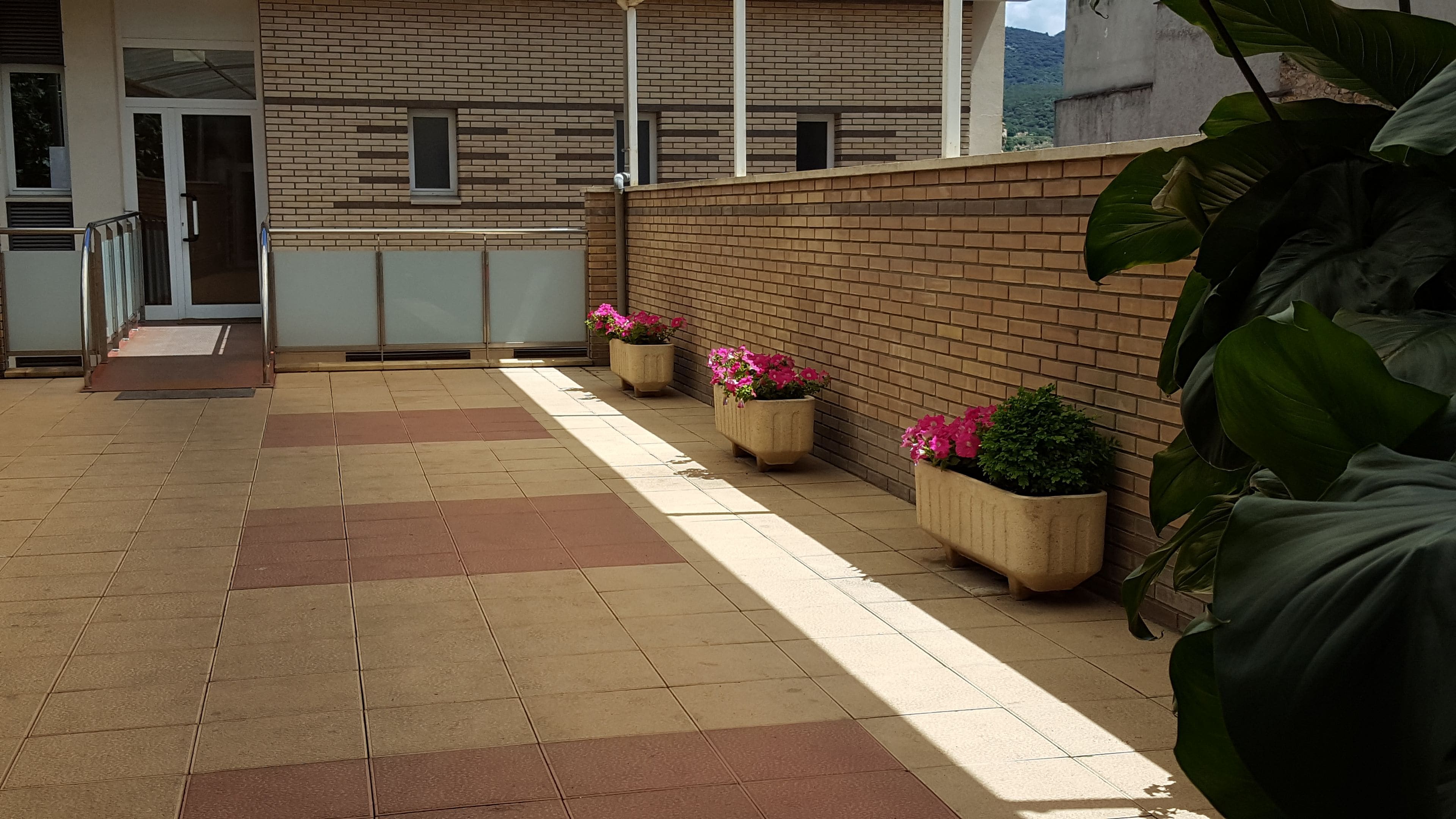 A covered outdoor area with a tiled floor, brick walls, and potted plants with pink flowers.