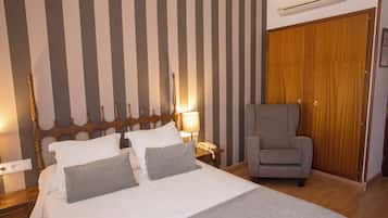 A hotel room with a bed, a chair, a nightstand, a lamp, and a wardrobe.