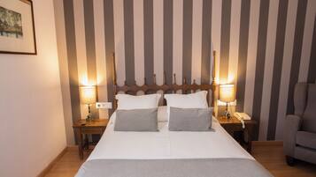 A hotel room with a large bed, two bedside tables, a chair, and a striped wall.