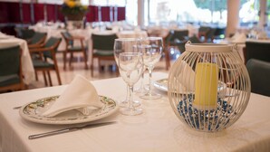 A dining table set with plates, glasses, and a candle in a well-lit room with large windows. - Segle XX (Tremp)