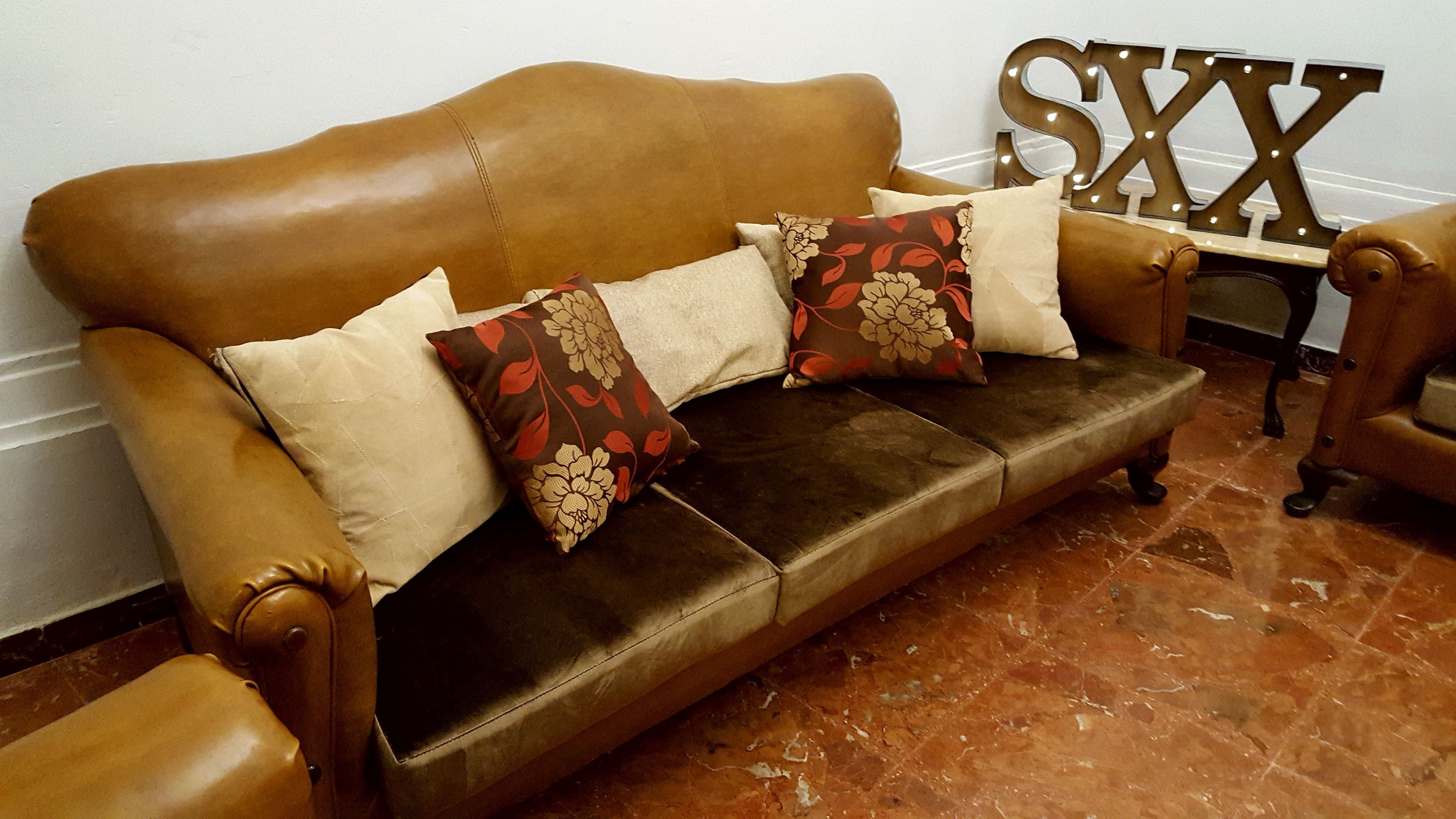 A brown leather sofa with floral cushions, a wooden side table with a 'SXX' sign, and a tiled floor.