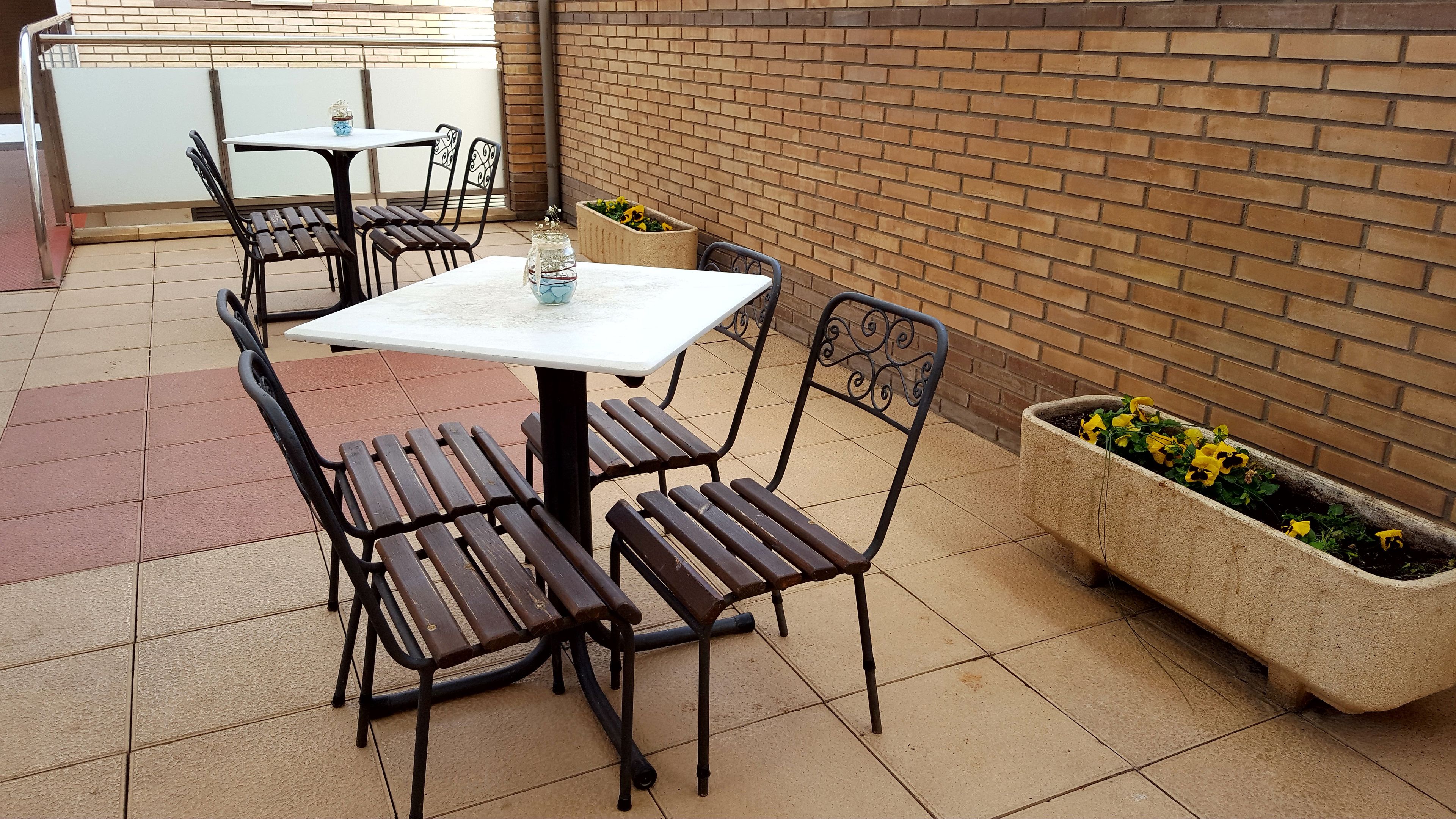 A patio area with a table and chairs, a planter with flowers, and a brick wall.
