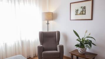 Um quarto com uma poltrona cinzenta, uma luminária, uma mesinha com uma planta e um quadro na parede.