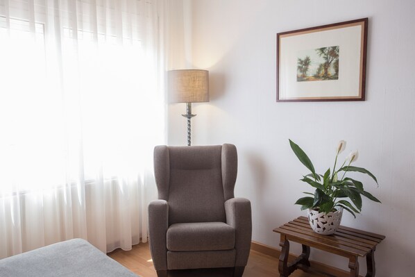 Una habitación con un sillón gris, una lámpara, una mesita con una planta y un cuadro en la pared.
