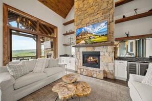 Uma sala de estar com lareira de pedra, uma televisão grande e vista para o exterior.