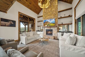 Un amplio salón con chimenea de piedra, un televisor grande y un comedor con vigas de madera y pared de piedra.