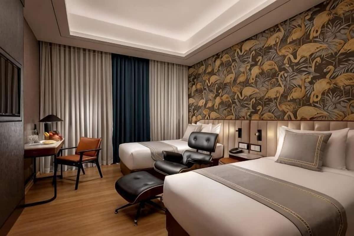 A hotel room with two beds, a desk, a chair, and a large patterned wall.