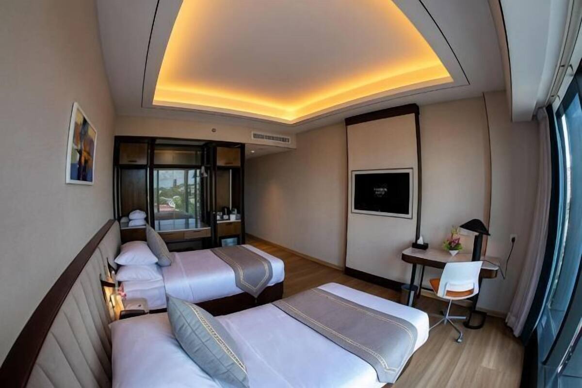 A hotel room with two beds, a desk, a chair, a TV, and a window.