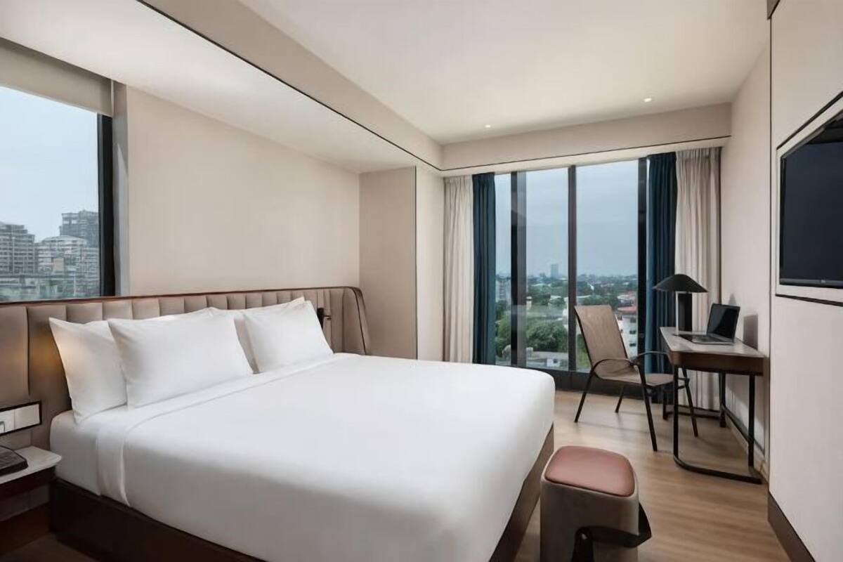 A hotel room with a large bed, a desk, a chair, and a view of the city.