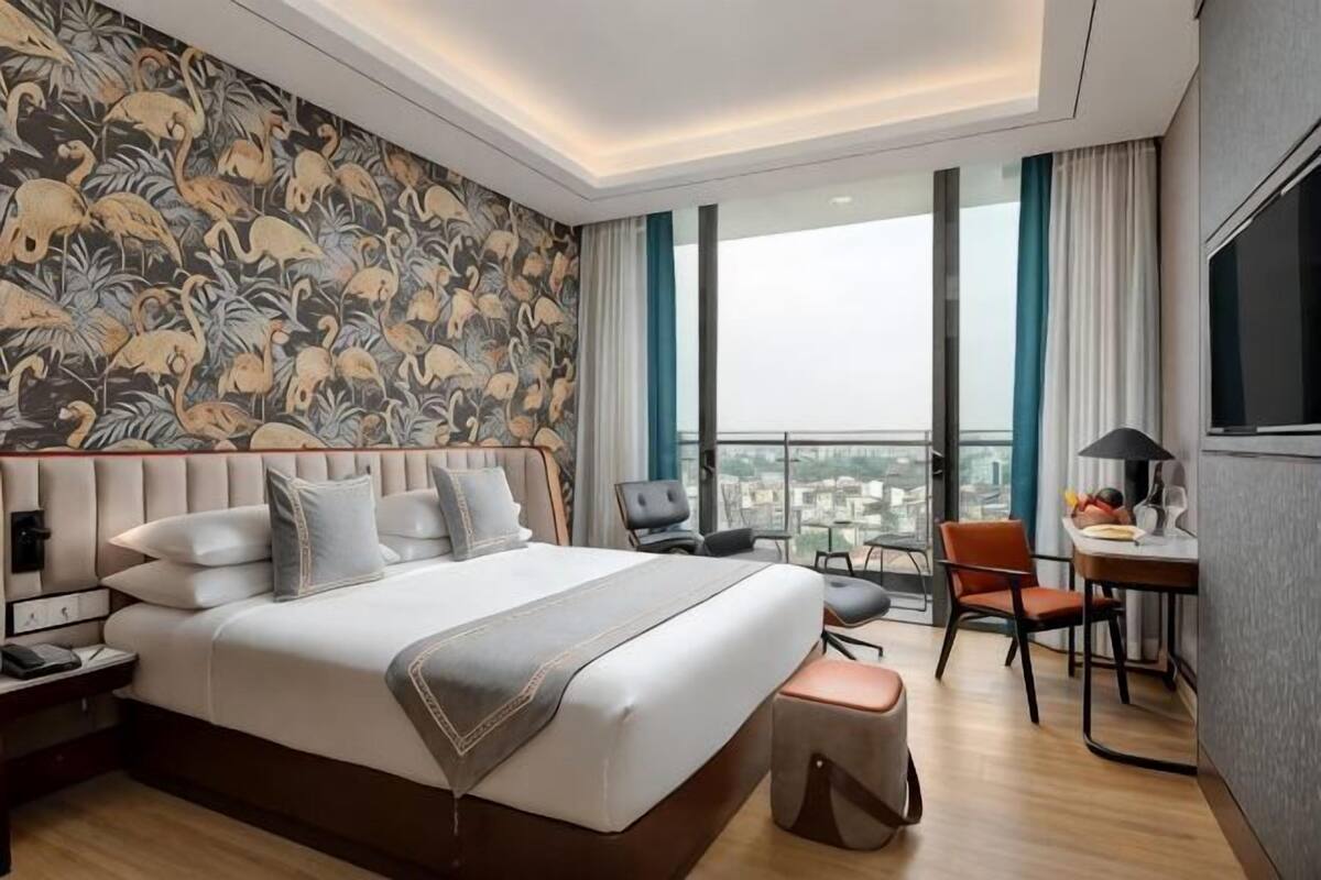 A hotel room with a large bed, a desk, a chair, and a view of the city.