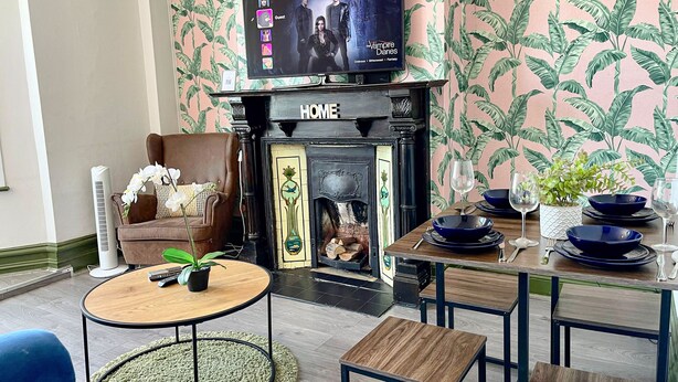 Un salon doté d’une cheminée, avec un téléviseur fixé au-dessus, et un coin repas avec de la vaisselle bleue.