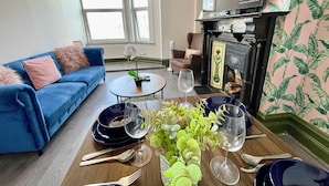 Un salon avec un canapé bleu, une table basse ornée d’une plante, une cheminée et un téléviseur diffusant une émission.