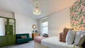 Une chambre à coucher avec un lit, un canapé vert, une commode, un miroir et une fenêtre.