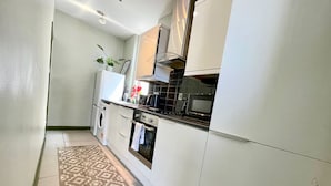Une cuisine moderne avec des meubles blancs, un four encastré, un four à micro-ondes et un lave-linge.
