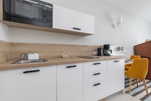 A modern kitchen with a microwave, sink, and white cabinets. There is a wooden countertop and a yellow chair.