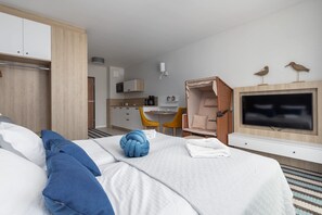 A modern hotel room with a bed, a TV, a desk, and a kitchenette.