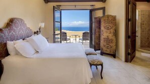 A bedroom with a large bed, a chair, a small table, and a view of the beach. - Pedregal Luca incredible Views with onsite staff (Cabo San Lucas)