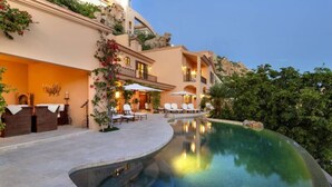 A hotel with a swimming pool, outdoor seating, and a mountainous backdrop. - Pedregal Luca incredible Views with onsite staff (Cabo San Lucas)