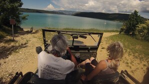 Un véhicule est garé sur un point de vue surplombant un lac, offrant une vue dégagée sur l’eau et les collines lointaines.