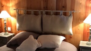 Une chambre à coucher avec une tête de lit en bois, deux lampes de chevet et un lit recouvert d’une couverture marron texturée et agrémenté d’oreillers.