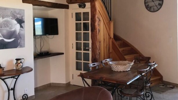 Un coin repas accueillant avec une table et des chaises en bois, un téléviseur fixé au mur et un escalier menant à l’étage supérieur.