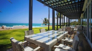 Un espacio de estar techado al aire libre con vista al océano, que incluye muebles de mimbre y una mesa de vidrio.