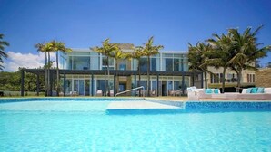 Un hotel moderno con una amplia piscina, palmeras y un cielo azul despejado.