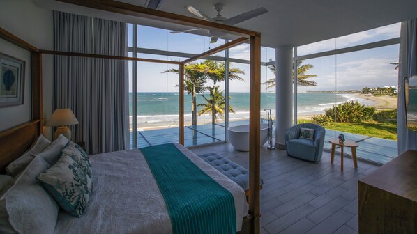 Une chambre avec un grand lit, une vue sur l’océan, un balcon avec un fauteuil et une baignoire.