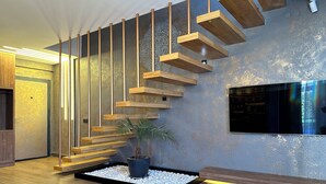A modern interior with a wooden staircase, a potted plant, and a flat-screen TV mounted on the wall. - DrVilla Suits (Serik)