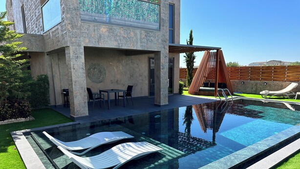 A modern outdoor pool area with a clear pool, lounge chairs, and a seating area with a table and chairs. - DrVilla Suits (Serik)