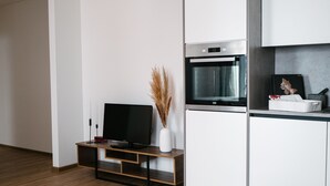 A modern kitchen with white cabinets, a built-in oven, and a flat-screen TV on a wooden stand.