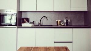 A modern kitchen with white cabinets, a built-in oven, a sink with a faucet, and a wooden table in the foreground.