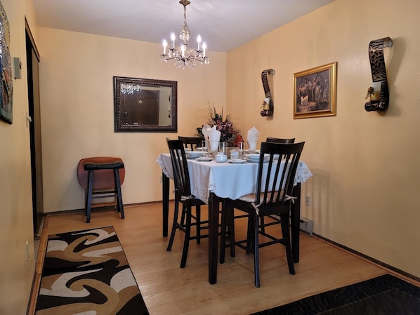 A dining area with a round table, chairs, a chandelier, a mirror, and wall decorations.