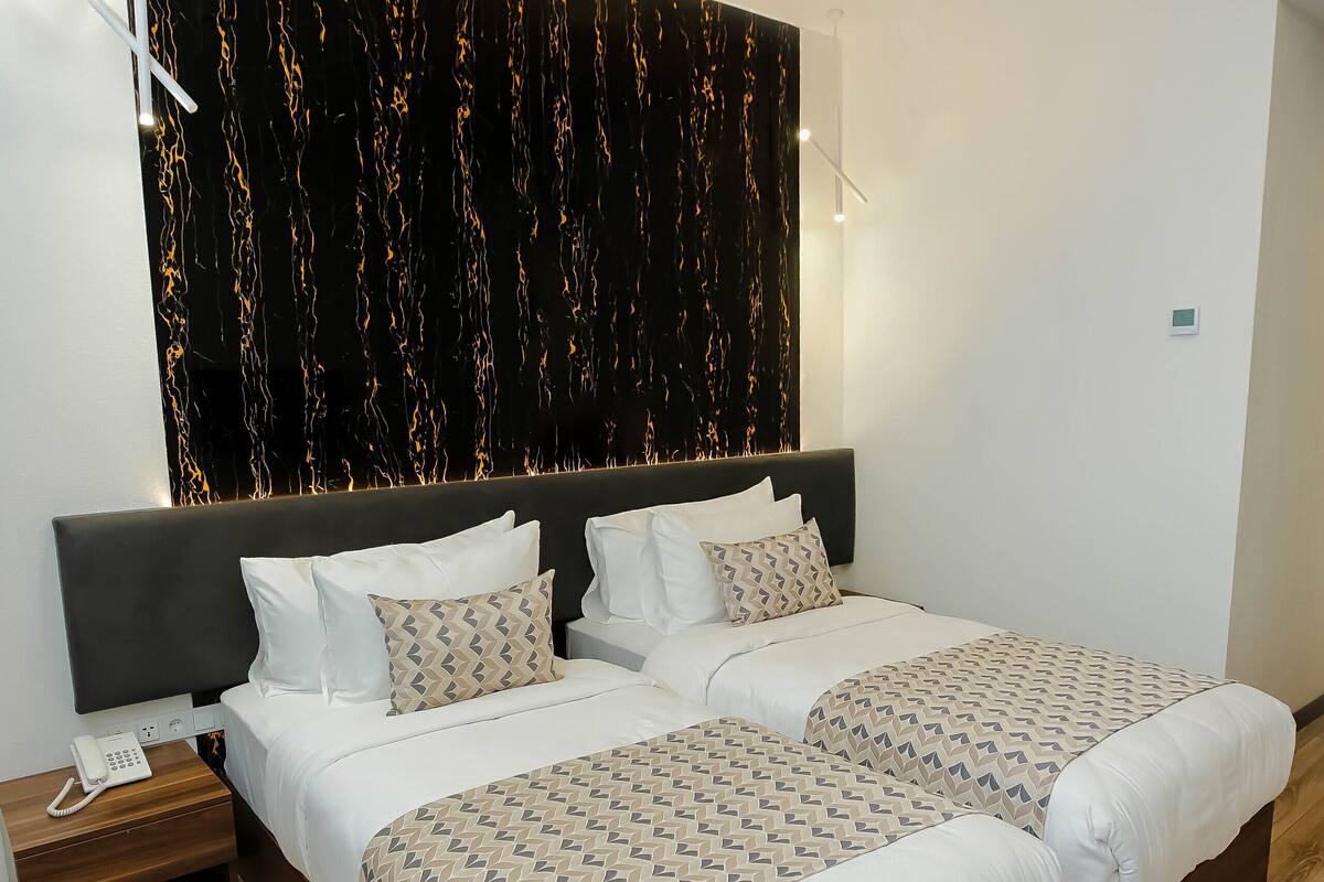 A modern hotel room with a large bed, bedside tables, and a decorative wall panel.