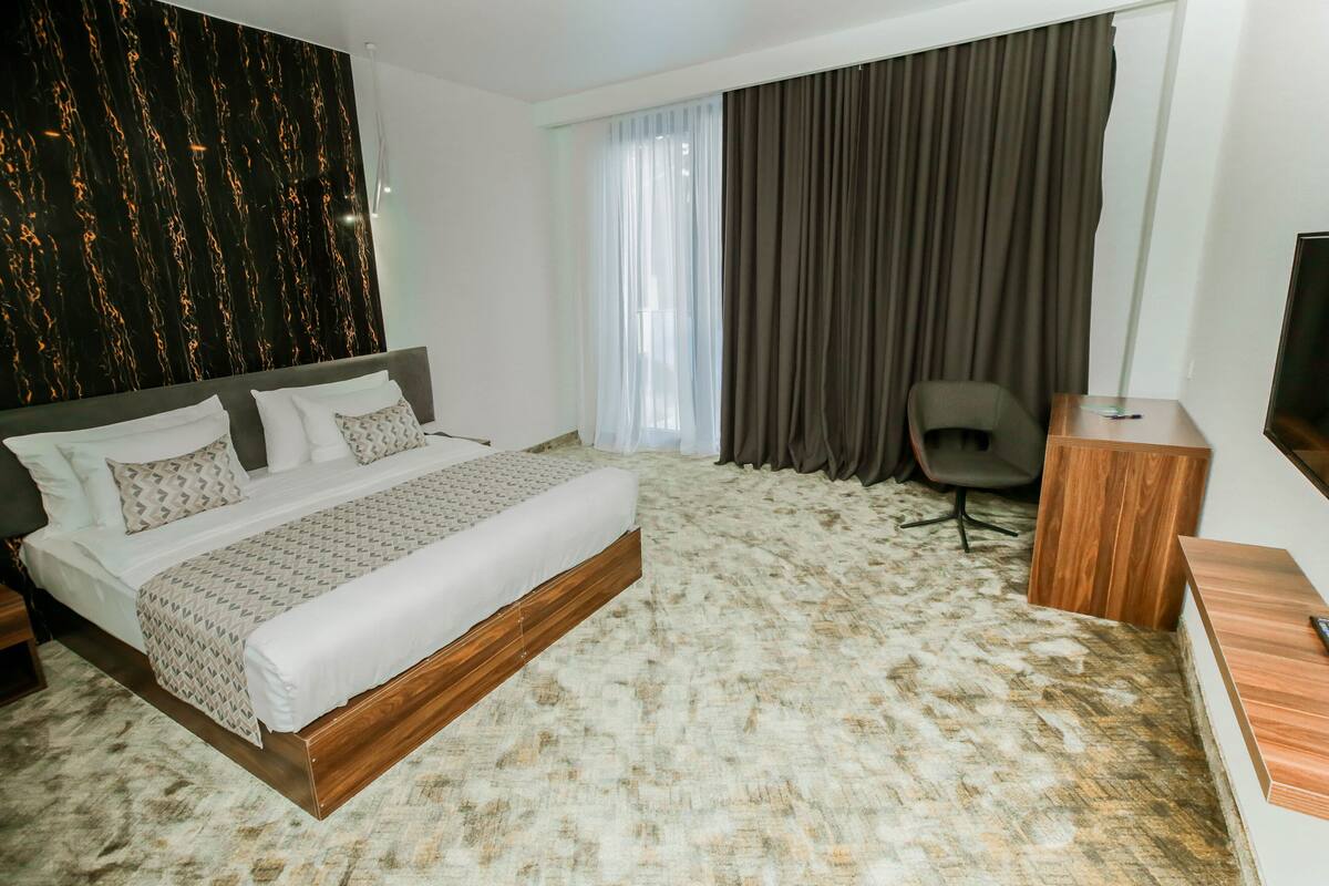 A hotel room with a large bed, a desk, a chair, a TV, and a view of the outdoors.