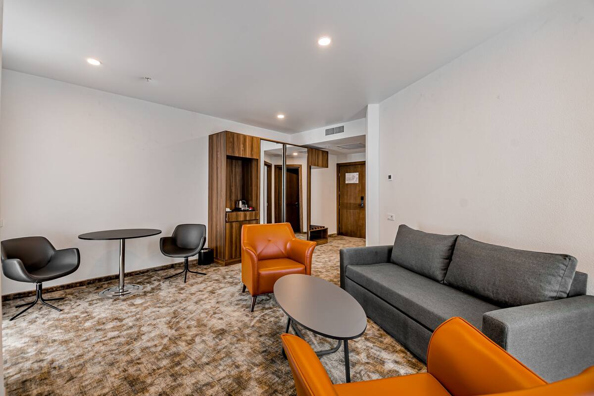 A modern living room with a grey sofa, orange armchairs, a small round table, and a wooden cabinet.