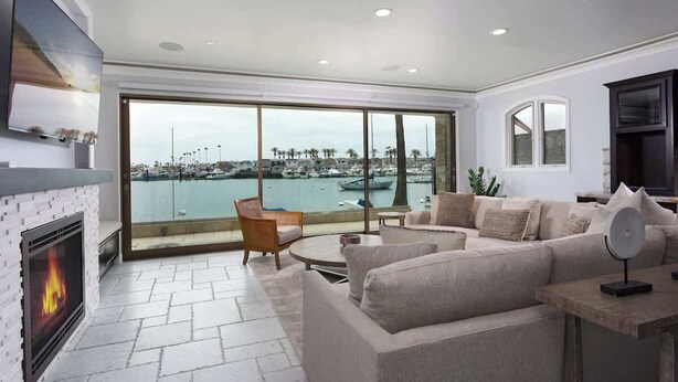 A modern living room with a fireplace, comfortable seating, and a large window overlooking a marina.