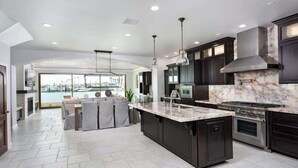 A modern kitchen with dark cabinetry, a large island, and a view to a pool.