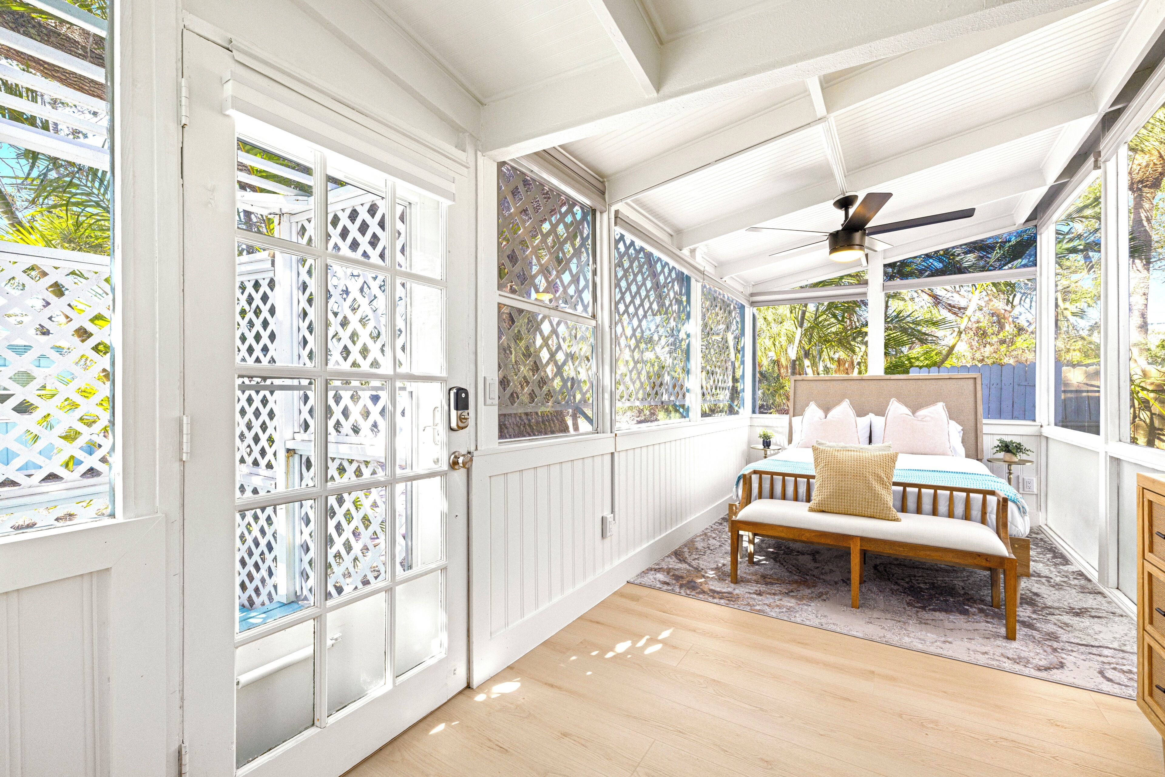 A sunlit room with a bed, a bench, and a ceiling fan.