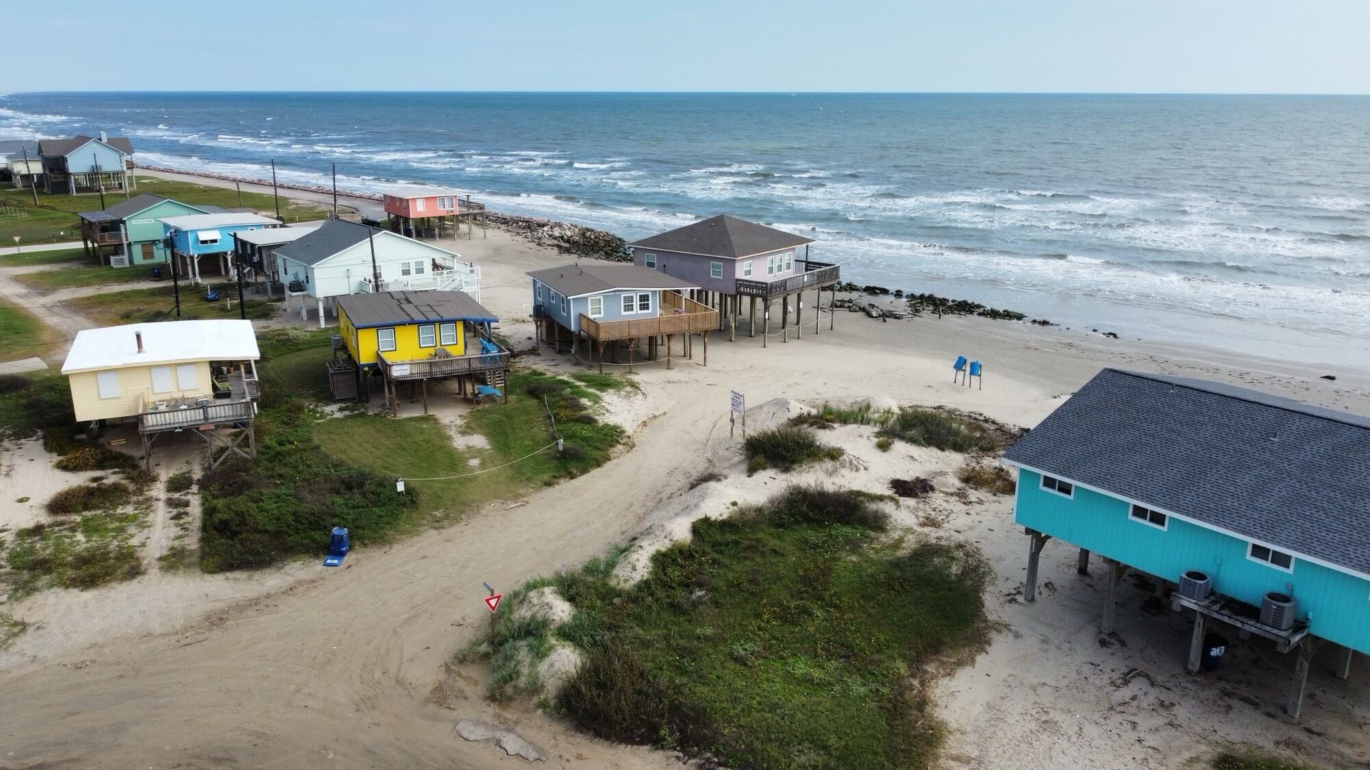 A coastal area with multiple houses and a beach. Houses are built on stilts over the sand.