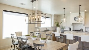 Una cocina moderna con una isla central, iluminación colgante y un comedor con sillas y una mesa.