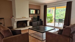 A living room with a fireplace, a television, and a balcony with a view of greenery. - Villa Provencale Avec Piscine Privee (Sainte-Maxime)