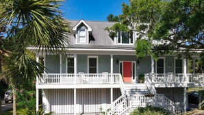 A two-story house with a red door, white railings, and a front porch. - Updated near beach home, outdoor paradise, sleeps 6! (Isle of Palms)