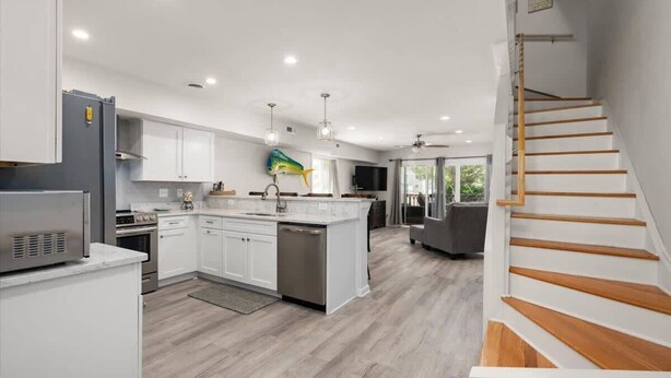 A modern kitchen with white cabinets, a central island, stainless steel appliances, and a wooden staircase. - Large Ocean City Waterfront Townhome w/ Boat Slip (Ocean City)