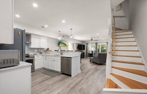 A modern kitchen with white cabinets, a central island, stainless steel appliances, and a wooden staircase.