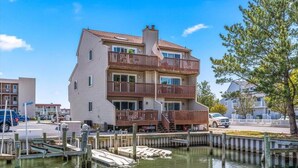 A multi-story building with a balcony, dock, and waterfront view. - Large Ocean City Waterfront Townhome w/ Boat Slip (Ocean City)