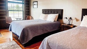A hotel room with two beds, a desk with a lamp, a chair, and a window with a view of trees. - {Big Timbers} Lodging next to North Entrance of Itasca State Park (Shevlin)