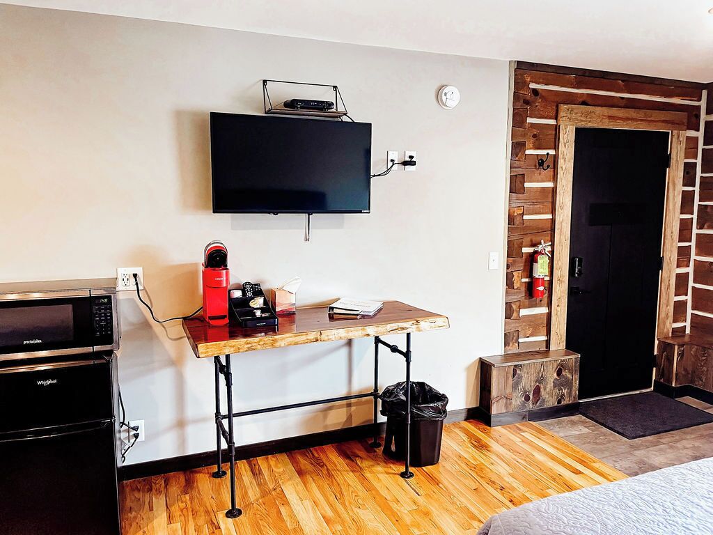 Une chambre compacte dotée d’un téléviseur à écran plat fixé au mur, d’une kitchenette équipée d’un four à micro-ondes, d’une machine à café et d’une petite poubelle.