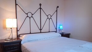 Ein ordentlich bezogenes Bett mit weißen Leinen, einem Metall-Kopfteil, einer Nachttischlampe und einem Nachttisch mit Lampe.