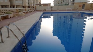 Ein Schwimmbecken mit glasklarer, blauer Wasseroberfläche, umgeben von einer gefliesten Liegefläche und einer niedrigen Mauer mit Pflanzkästen.